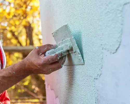 Person applying textured thin coat render to a wall
